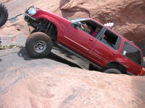 1997 Ford Ranger - Modified red SUV tackling a challenging rocky terrain, with a tow strap attached.