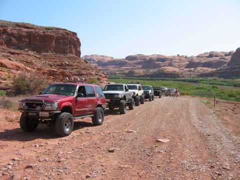 1997 Ford Ranger - A convoy of modified off-road vehicles travels down a dusty trail through a canyon landscape.