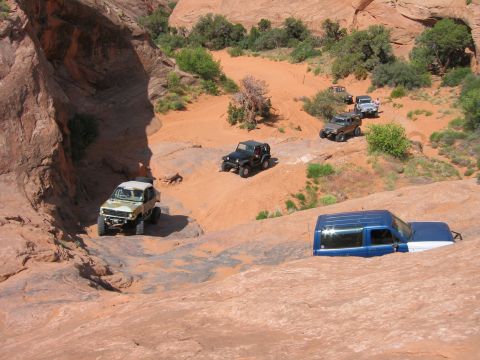 1997 Ford Ranger - Several off-road vehicles traverse a challenging sandy and rocky landscape, with one blue and white SUV stuck in the sand.
