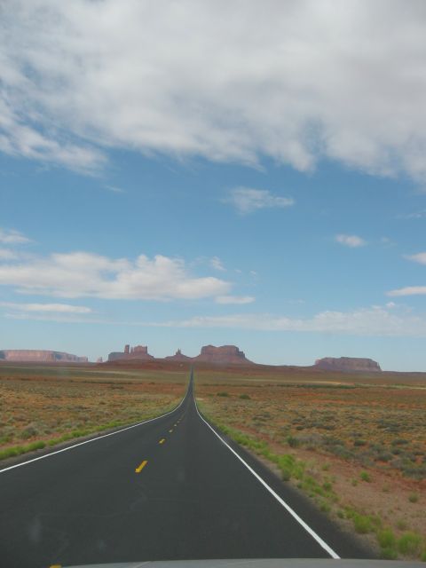 1997 Ford Ranger - A long, empty road leads through a vast desert landscape towards distant rock formations under a partly cloudy sky.