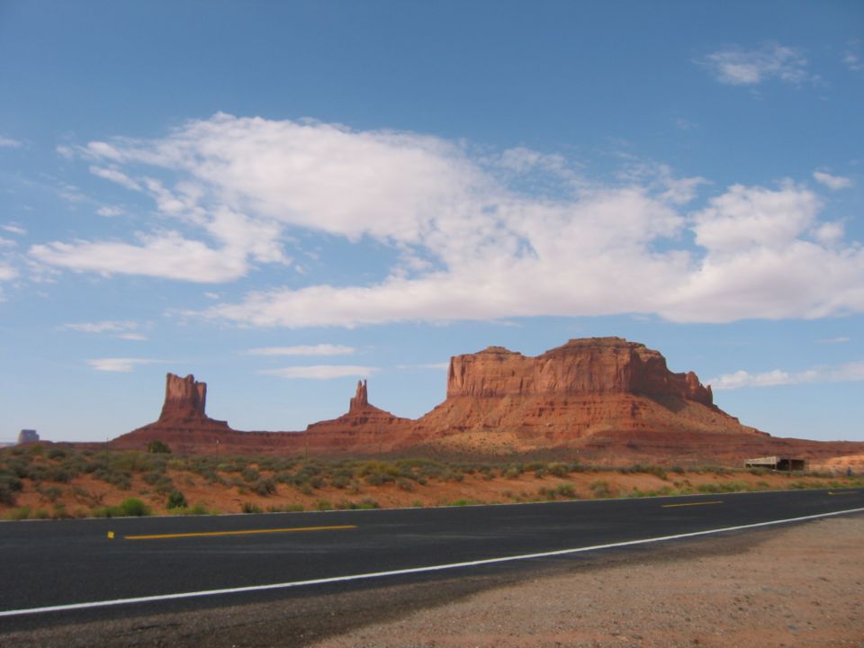Desert landscape with mesas and a road under a blue sky with clouds