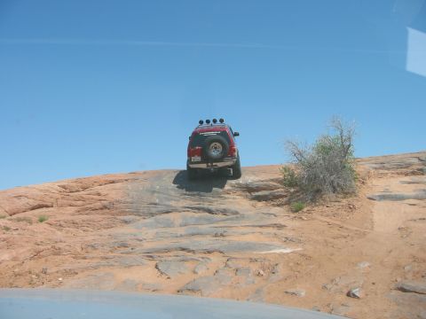 1997 Ford Ranger - A red SUV navigates a challenging rocky incline on a sunny day.