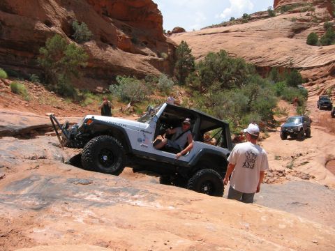 1997 Ford Ranger - A white Jeep Wrangler Rubicon tackles a challenging off-road course in a desert landscape, with other vehicles following behind.