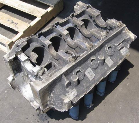 1972 Ford Ranchero - A V8 engine block foundry pattern or sand-core assembly resting on pavement beside a wooden pallet, shot from above so the main bearing bul…