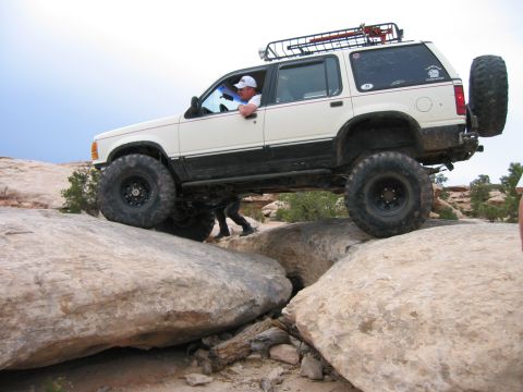 1997 Ford Ranger - This white SUV is shown off-roading over large rocks, with a driver behind the wheel and a roof rack installed.