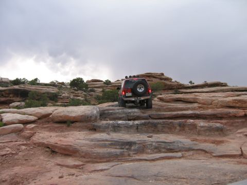 1997 Ford Ranger - A red SUV navigates a challenging rocky trail under a cloudy sky.