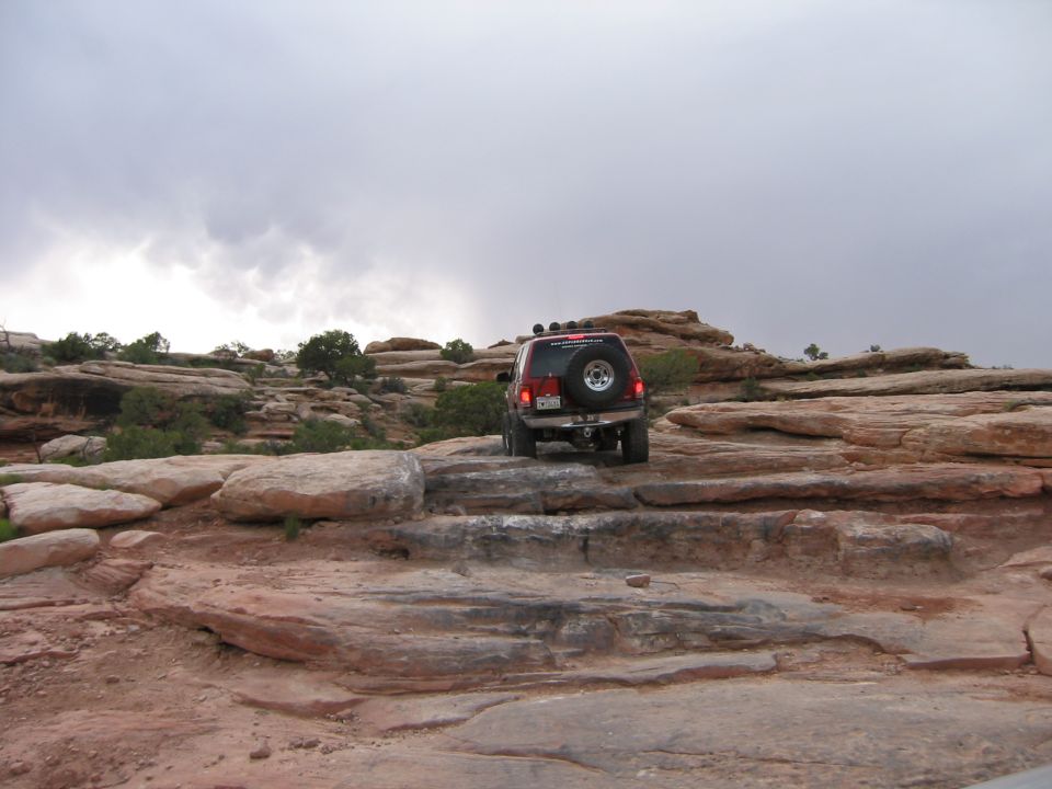 red SUV climbing over rocks on a trail
