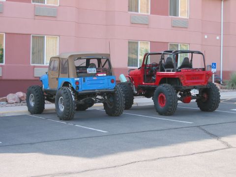 1997 Ford Ranger - Two heavily modified off-road vehicles are parked side-by-side in front of a pink building.