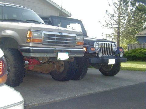 1994 Ford Explorer - Two modified SUVs, a Ford Explorer and a Jeep Wrangler, are parked side-by-side on a paved surface.