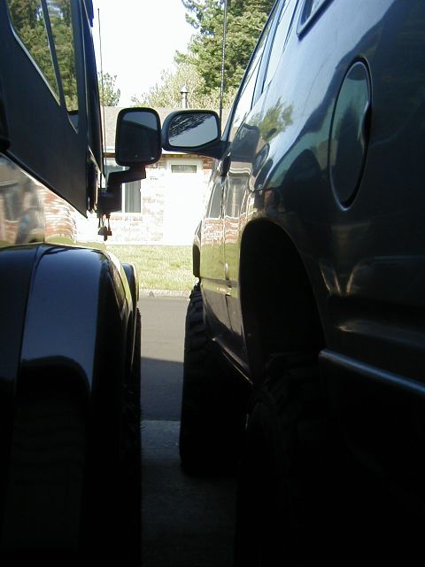 1994 Ford Explorer - The side of a dark SUV is visible next to another vehicle, with a house and trees in the background.