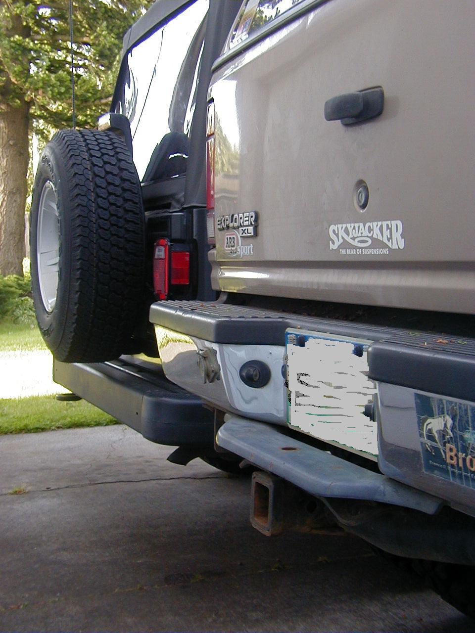 Rear corner of a tan Ford Explorer XL with spare carrier and Skyjacker decal