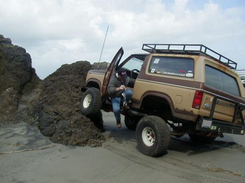 1994 Ford Explorer - Ford Bronco tackles challenging beach terrain with its driver exiting the vehicle.