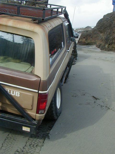 1994 Ford Explorer - This modified Ford Bronco is navigating a sandy beach with rocky outcrops.