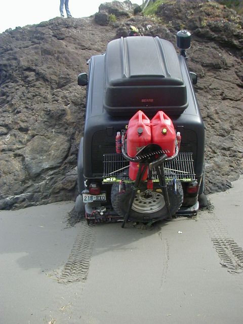 1994 Ford Explorer - A black SUV is partially submerged in sand, its rear laden with fuel cans and a spare tire.
