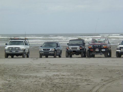 1994 Ford Explorer - A group of off-road vehicles are lined up on the sand with the ocean in the background.