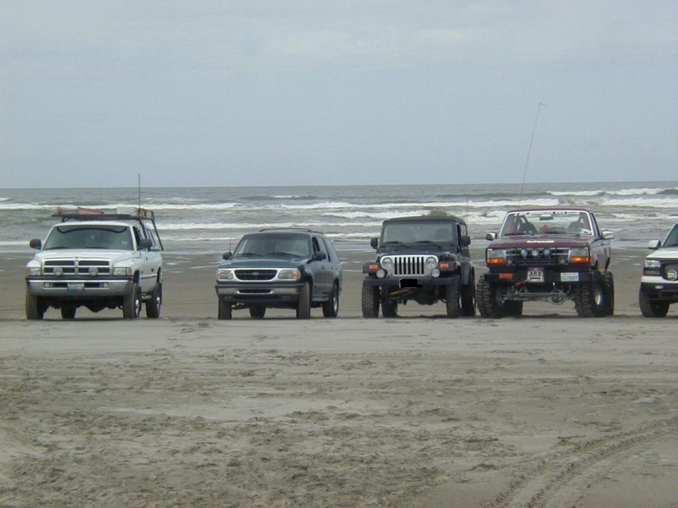 White Dodge Ram, green Explorer, black Jeep Wrangler and maroon Bronco parked on a beach