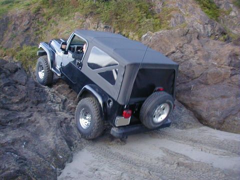 1994 Ford Explorer - A black Jeep Wrangler navigates a rocky coastal path with sandy patches.