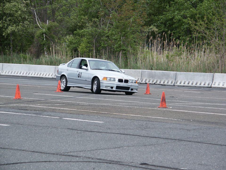 Silver BMW E36 sedan with number 61 on the door, navigating an autocross course with orange cones