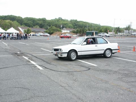 2001 Mercury Grand Marquis - White BMW E30 coupe navigates an autocross course with other vehicles and tents visible.