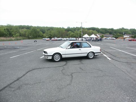 2001 Mercury Grand Marquis - A white BMW E30 coupe is seen on a paved lot during an event with other vehicles and tents visible.