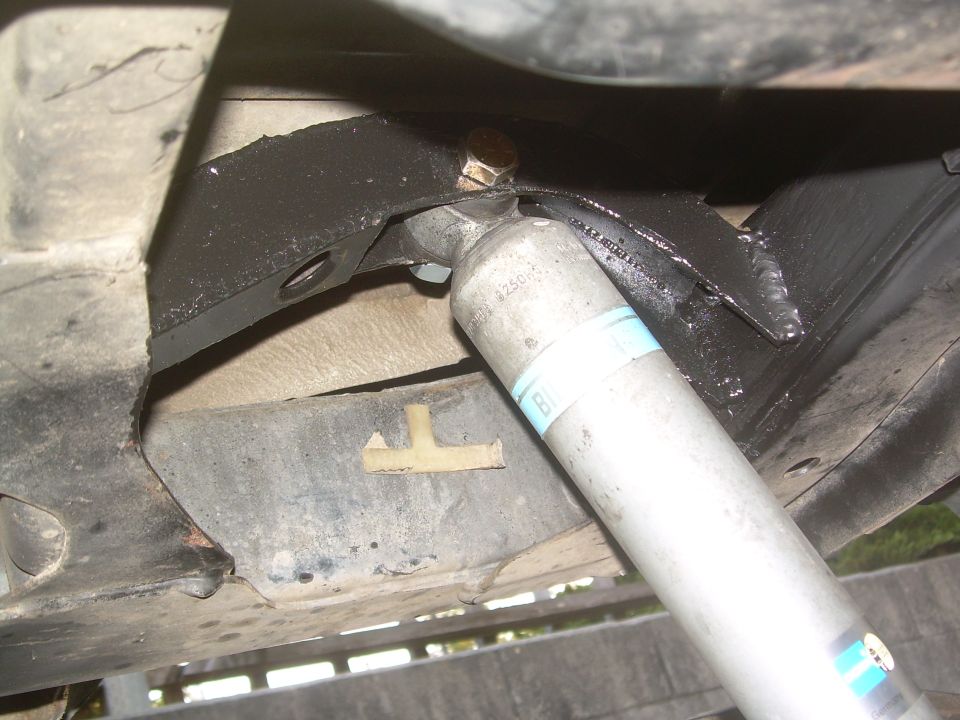 Close-up of a rear shock absorber and black metal mounting bracket on a vehicle's undercarriage