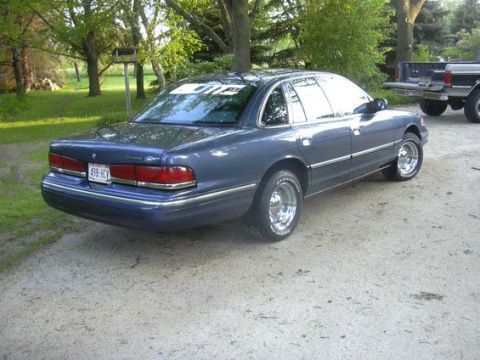 1996 Ford Crown Victoria - A blue 1996 Ford Crown Victoria is parked on a dirt road, with a pickup truck visible in the background.