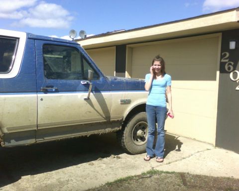 1989 Ford Bronco - A muddy blue and white 1989 Ford Bronco is parked in front of a garage with a young woman standing beside it.