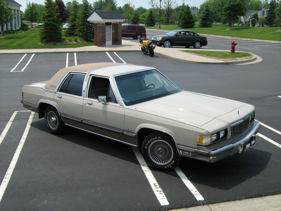 Tan Mercury sedan parked diagonally with a motorcycle in background