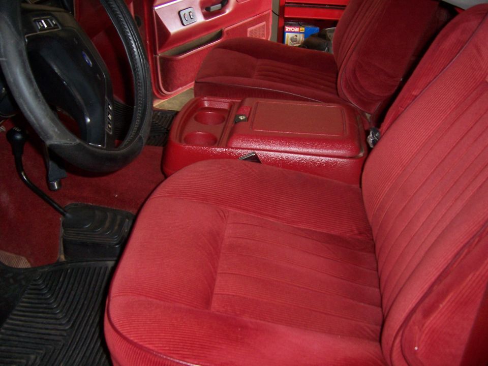 Red cloth interior of a Ford Bronco with bench seat, center console with cupholders, and black steering wheel