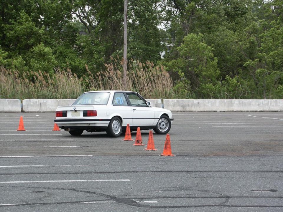 White BMW E30 coupe navigating an autocross course with orange cones