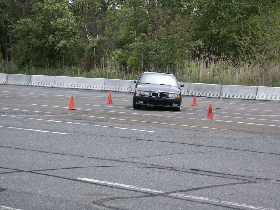 Black BMW E36 coupe navigating an autocross course with orange cones