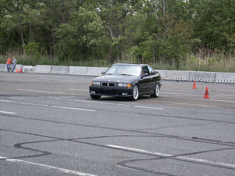 Black BMW E36 coupe driving on a paved track with orange cones