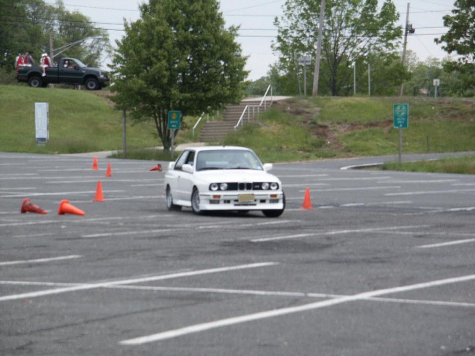 White BMW E30 M3 with front spoiler and fog lights, navigating a cone course