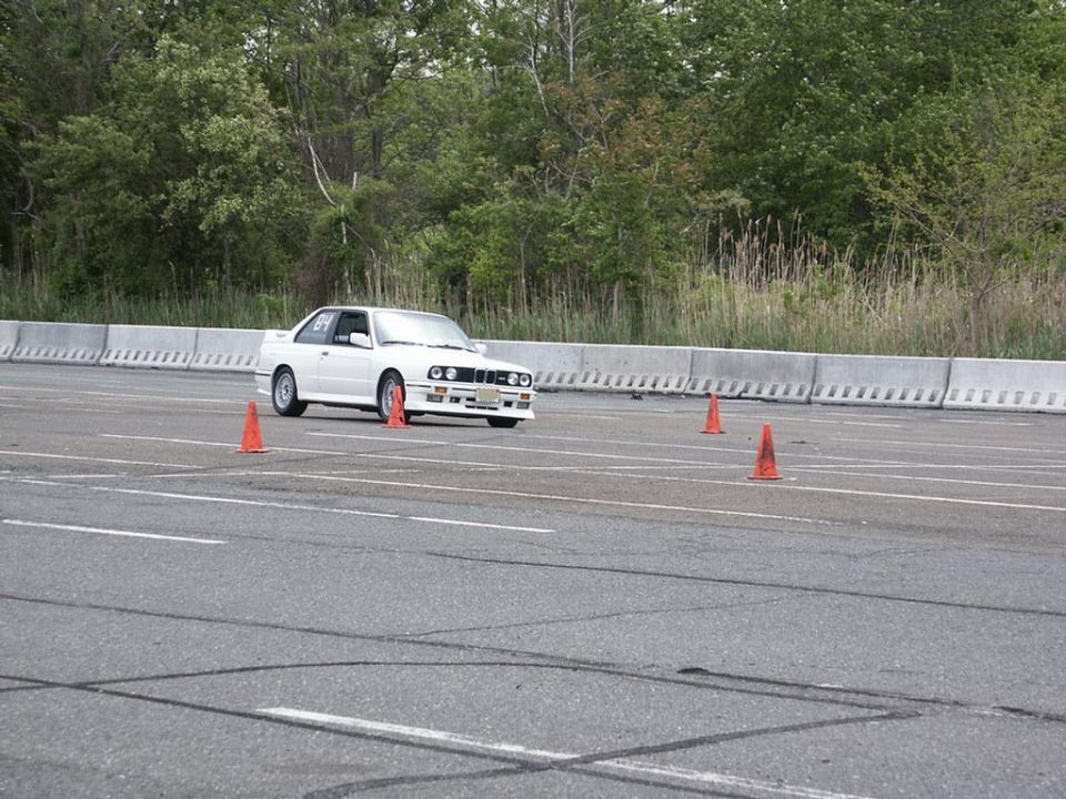 White BMW E30 M3 navigating a course marked by orange cones on asphalt