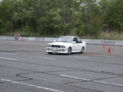 2001 Mercury Grand Marquis - A white BMW E30 M3 navigates an autocross course, indicated by orange cones and tire marks on the asphalt.