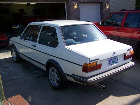 1984 Volkswagen Jetta - This white 1984 Volkswagen Jetta is seen from the rear 3/4 angle, with a red SUV parked nearby.