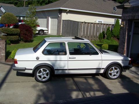 1984 Volkswagen Jetta - A white 1984 Volkswagen Jetta is parked in a driveway next to a house and fence. Another white car is visible in the background.