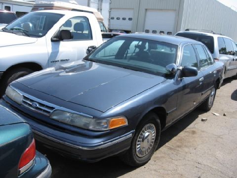 2003 Ford Crown Victoria - A dark blue 2003 Ford Crown Victoria is parked outdoors with other vehicles nearby.