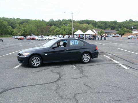 2001 Mercury Grand Marquis - A dark sedan with blue numbers on its rear window participates in an autocross event, with other vehicles and tents visible in the backgrou…
