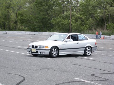 2001 Mercury Grand Marquis - A white BMW coupe with the number 100 visible on its rear window is seen on an asphalt track during an event.