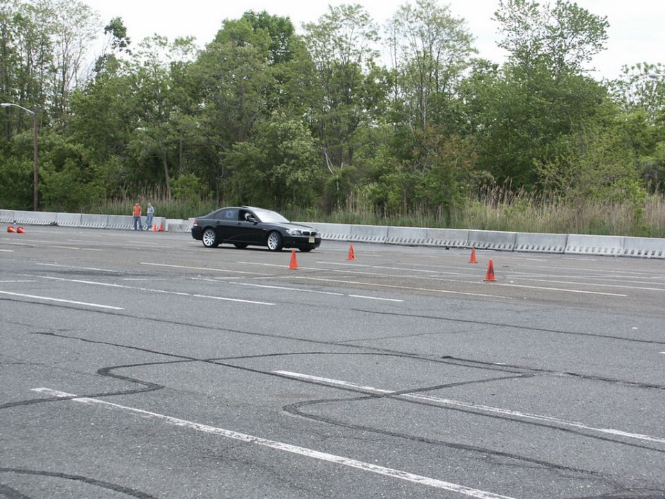 Black sedan driving on a track with orange cones. The car appears to be a BMW 3 Series