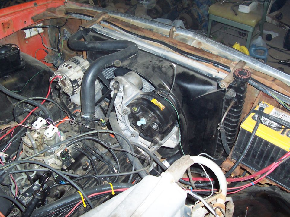 Engine bay with orange fender, alternator, radiator, and battery. Wires and hoses are visible