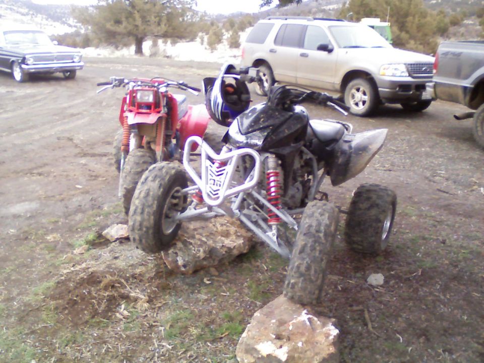 Black sport quad ATV with red shocks parked on rocks in a dirt lot