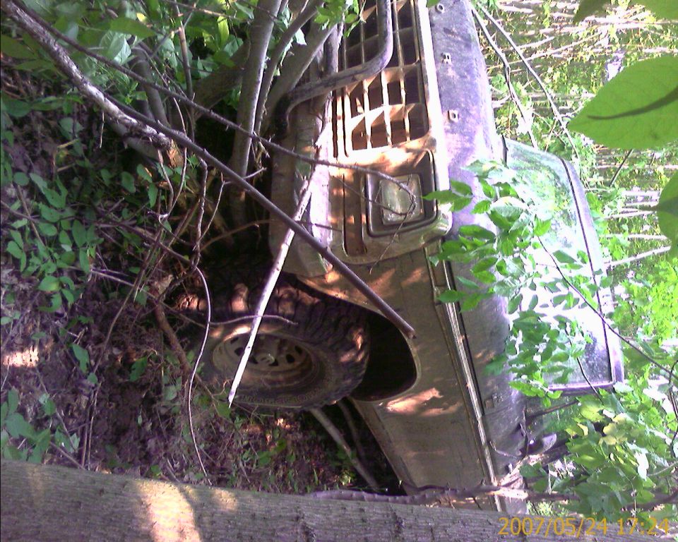 1979 Ford F-250 overturned in woods, front grille and tire visible