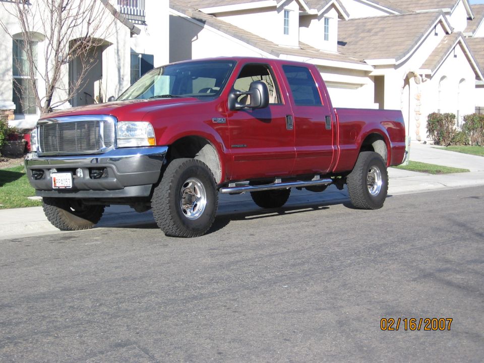 Lifted red Ford Super Duty crew cab with chrome grille, front 3/4 view on a street
