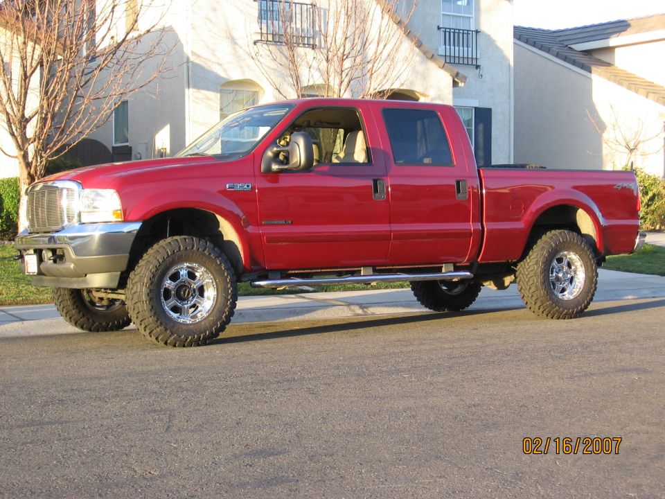 Red Ford F-350 Super Duty crew cab pickup on chrome wheels and mud tires, driver-side view