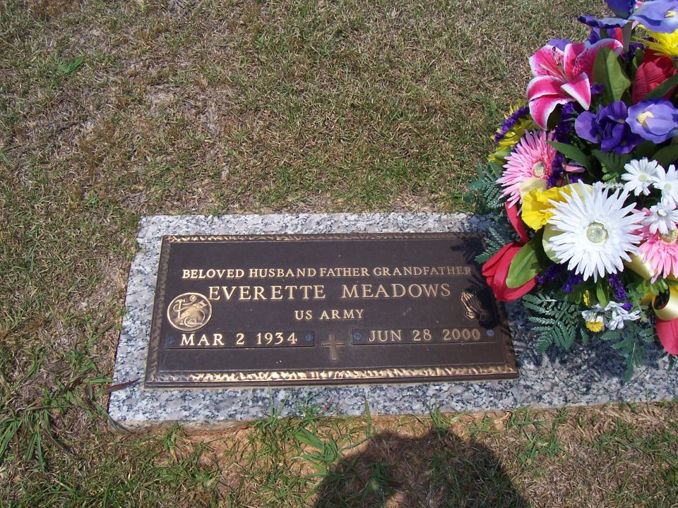 Gravestone with text for Everette Meadows, born March 2, 1934, died June 28, 2000, and US Army insignia, next to a floral arrangement