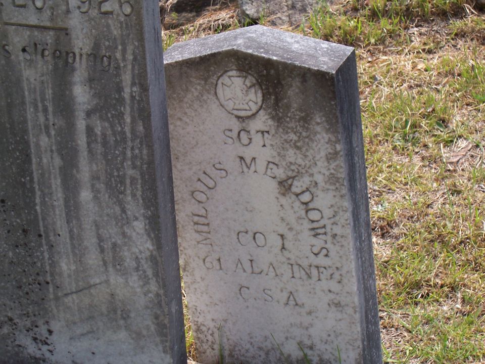 Two weathered gravestones in a grassy area. The right gravestone has text including 'SGT MILOUS MEADOWS CO 1 61 ALA INF C.S.A.' and a circular emblem
