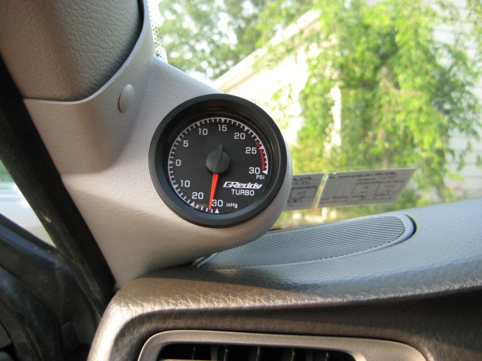 Interior view of a car's dashboard with a GReddy turbo gauge mounted on the A-pillar