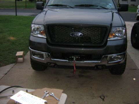 1986 Ford Bronco - Frontal view of a dark gray Ford F-150 truck, a prominent black grille with the Ford emblem and a chrome bumper.